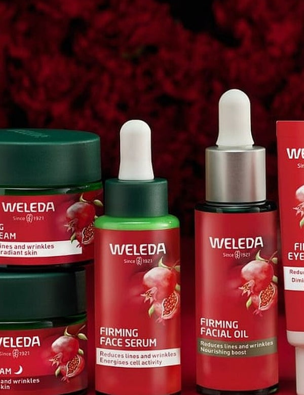 Weleda Pomegranate Firming face care range arranged against deep red florals, including night cream, day cream, serum, facial oil and eye cream.