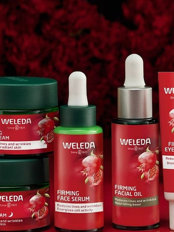 Weleda Pomegranate Firming face care range arranged against deep red florals, including night cream, day cream, serum, facial oil and eye cream.