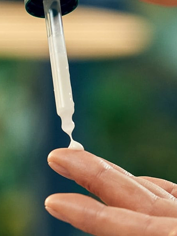 Firming face serum pipette being squeezed onto a finger before application.