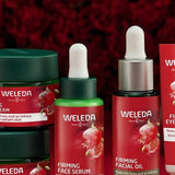 Weleda Pomegranate Firming facial-care range arranged against deep red flowers, including cream jars, serum, facial oil and eye cream.