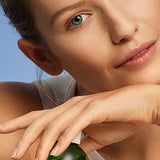 Young woman with clear skin posing with Weleda Refining Toner against a soft blue studio background.