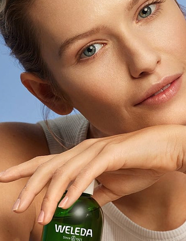 Young woman with clear skin posing with Weleda Refining Toner against a soft blue studio background.
