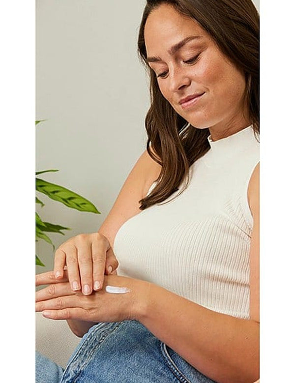Woman in a white sleeveless top applying Weleda Sea Buckthorn Replenishing Hand Cream across the back of one hand.