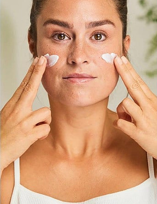 Woman applying Weleda Sensitive Soothing Moisturiser to both cheeks with her fingertips.