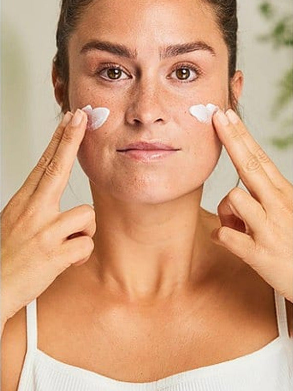 Woman applying Weleda Sensitive Soothing Moisturiser to both cheeks with her fingertips.