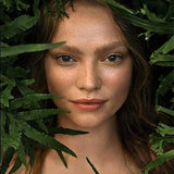 Close portrait of a woman framed by lush green leaves for the Weleda Skin Food range.