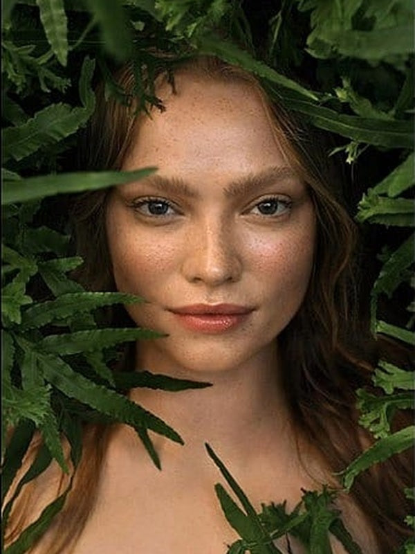 Close portrait of a woman framed by lush green leaves for the Weleda Skin Food range.