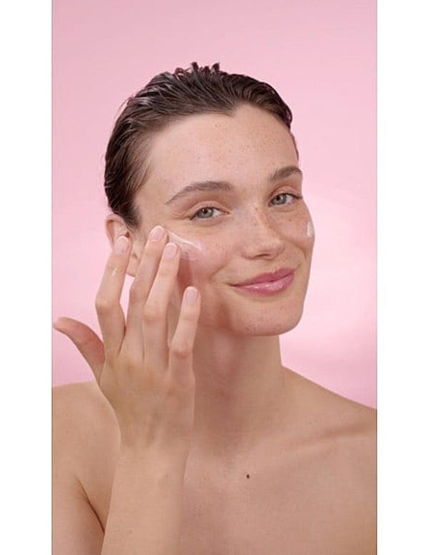 Woman applying Smoothing Wild Rose & White Tea cream on her face in a pink background.