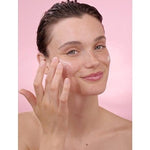 Woman applying Smoothing Wild Rose & White Tea eye cream on her face in a pink background.