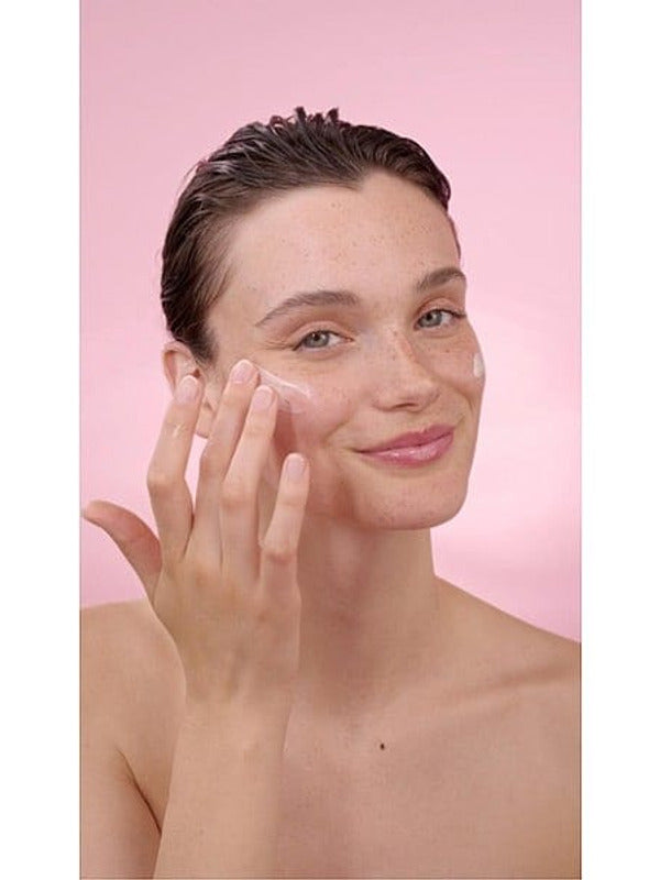 Woman applying Smoothing Wild Rose & White Tea eye cream on her face in a pink background.