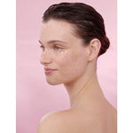 Woman's profile with Smoothing Wild Rose & White Tea cream on her face in a pink background.