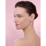 Woman's profile with Smoothing Wild Rose & White Tea cream on her face in a pink background.