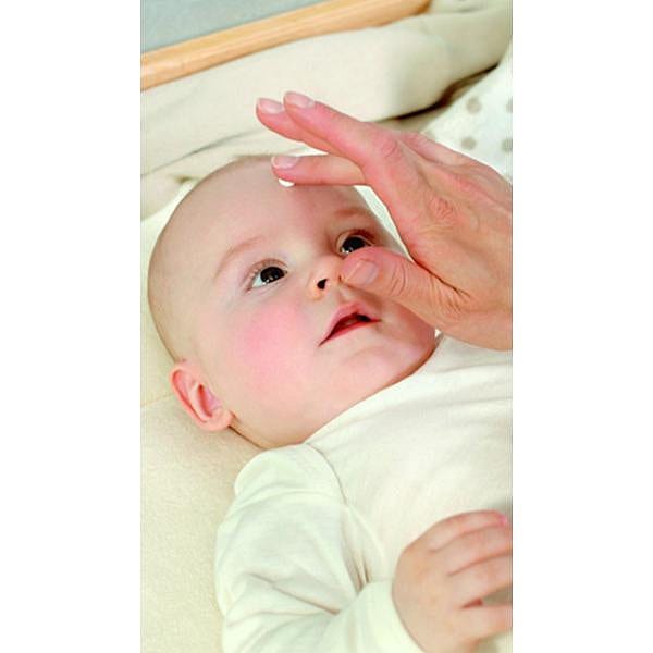 Baby lying down and hand applying cream to his face.