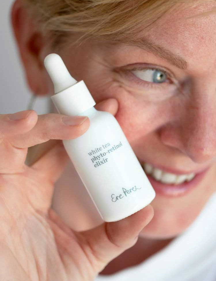 A person smiles while holding the Ere Perez White Tea Phyto-Retinol Elixir 30ml, displaying this gentle bakuchiol serum close to their face.
