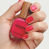 A hand holds Sienna Byron Bay Nail Polish - Wonder, a bright fuchsia pink, plant-derived nail polish. Nails match the color; the wooden cap highlights its toxin-free formula.