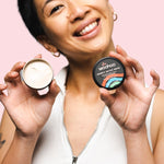 Smiling woman holding an open WooHoo Armpit Detox Mask tin