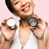 Smiling woman holding an open WooHoo Armpit Detox Mask tin