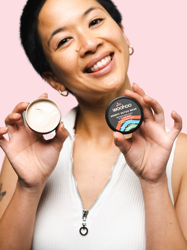 Smiling woman holding an open WooHoo Armpit Detox Mask tin
