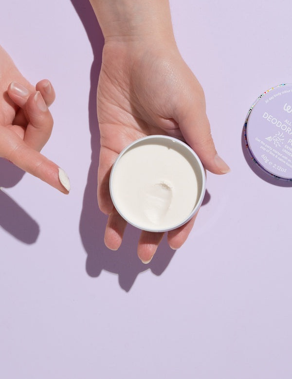 Open WooHoo Pop deodorant paste held in two hands against a purple background