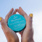 Hands holding WooHoo Surf deodorant paste against a blue sky