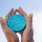 Hands holding WooHoo Surf deodorant paste against a blue sky