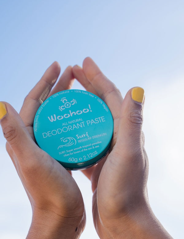 Hands holding WooHoo Surf deodorant paste against a blue sky