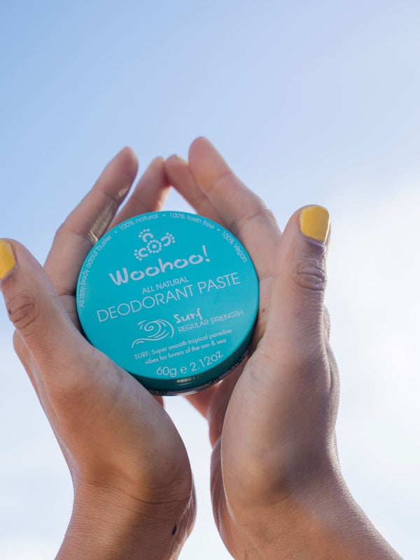 Hands holding WooHoo Surf deodorant paste against a blue sky