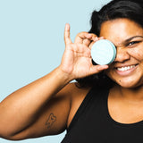 Smiling woman holding WooHoo Surf deodorant paste beside her face