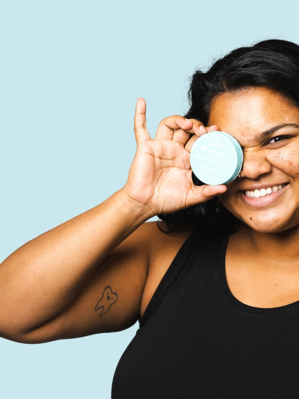 Smiling woman holding WooHoo Surf deodorant paste beside her face