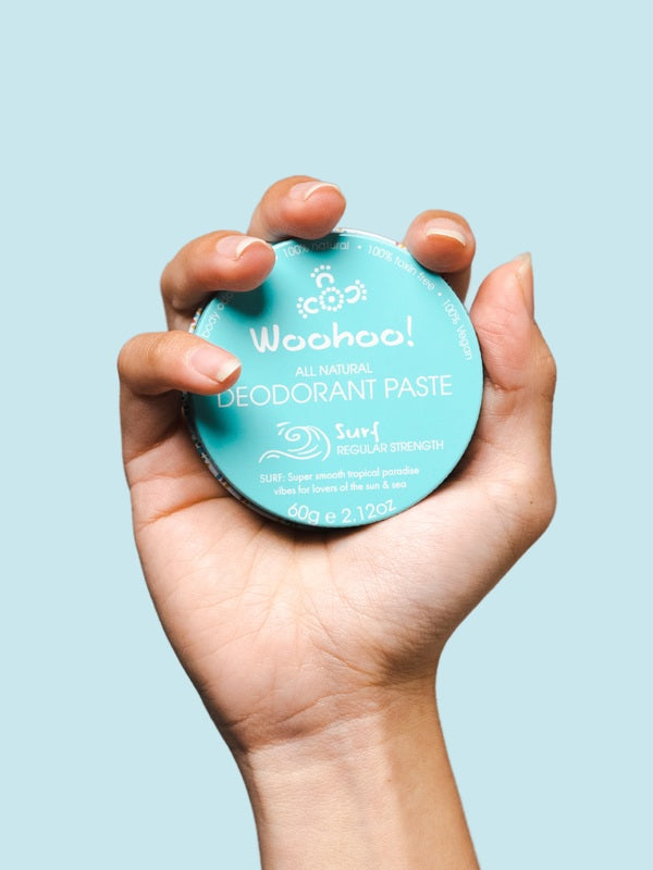 WooHoo Surf natural deodorant paste held in a hand against a blue background