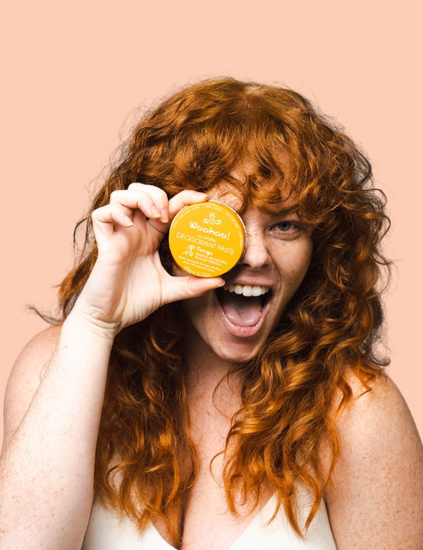 Smiling woman holding WooHoo Tango deodorant paste beside her face