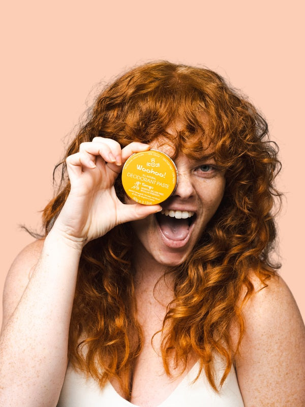 Smiling woman holding WooHoo Tango deodorant paste beside her face