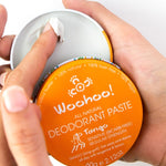Hands holding an open tin of WooHoo Tango deodorant paste