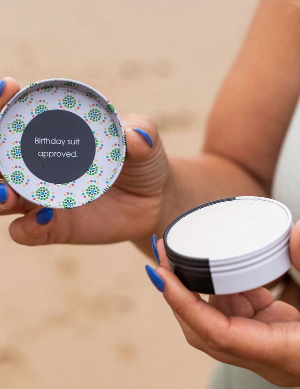 Hands holding an open tin of WooHoo Tux deodorant paste