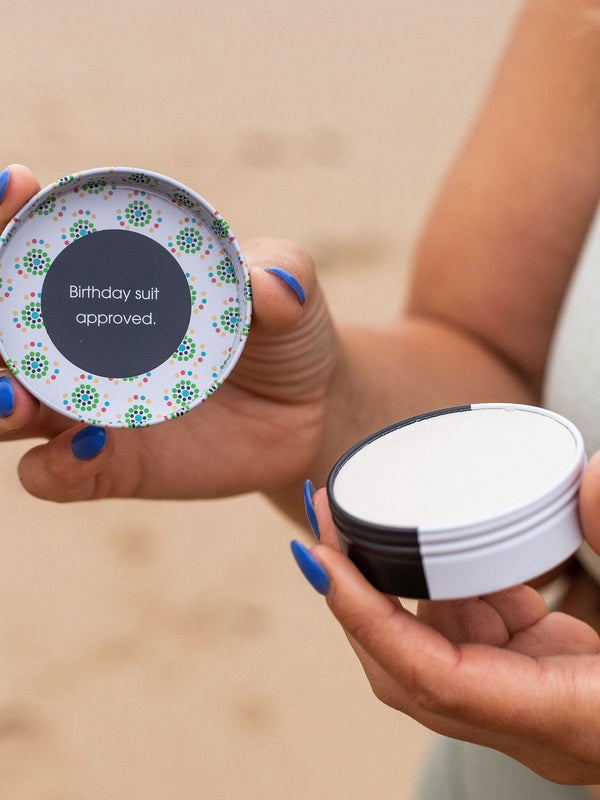 Hands holding an open tin of WooHoo Tux deodorant paste