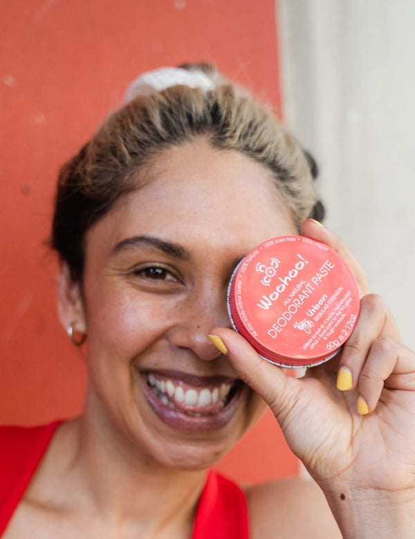Smiling woman holding WooHoo Urban deodorant paste beside her face against a red background
