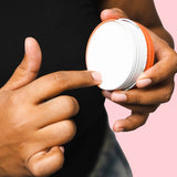 Hand scooping cream from an open tin of WooHoo Urban natural deodorant paste