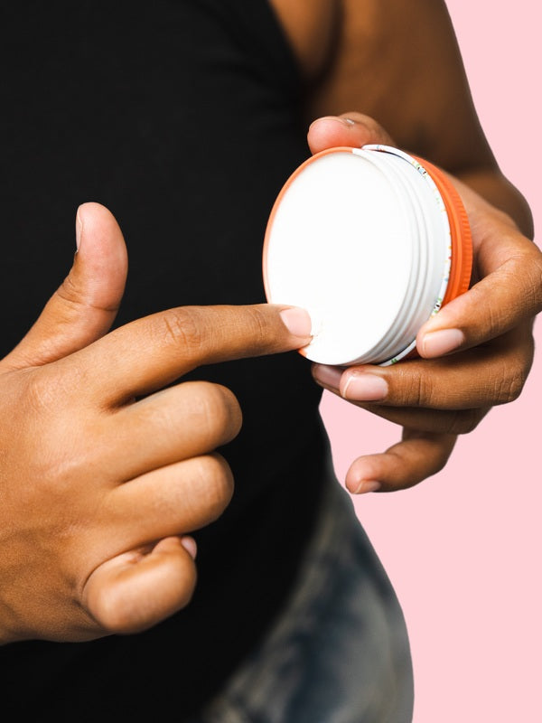 Hand scooping cream from an open tin of WooHoo Urban natural deodorant paste