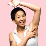 Woman applying WooHoo Urban deodorant paste to her underarm against a pink background