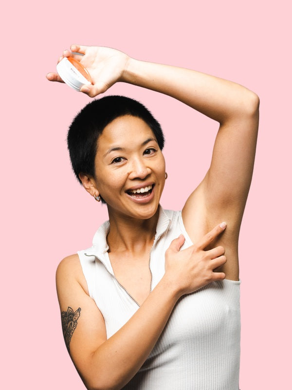 Woman applying WooHoo Urban deodorant paste to her underarm against a pink background