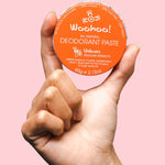 WooHoo Urban natural deodorant paste held in a hand against a pink background