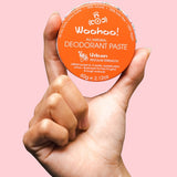WooHoo Urban natural deodorant paste held in a hand against a pink background