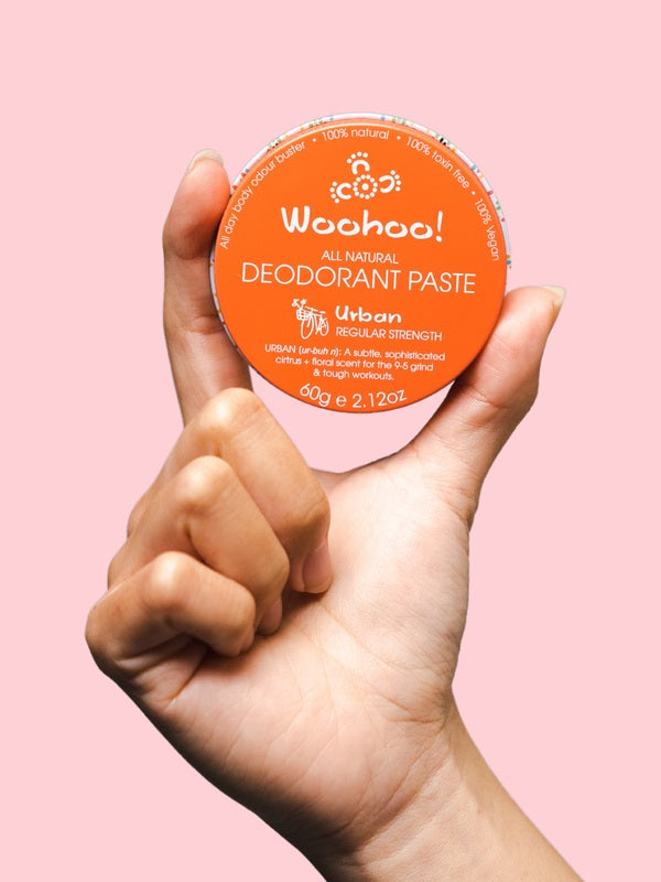 WooHoo Urban natural deodorant paste held in a hand against a pink background