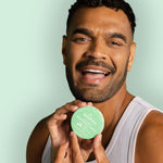 Smiling man holding WooHoo Wild natural deodorant paste beside his face