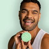 Smiling man holding WooHoo Wild natural deodorant paste beside his face