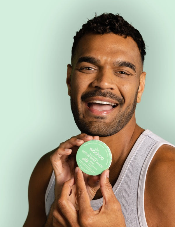 Smiling man holding WooHoo Wild natural deodorant paste beside his face