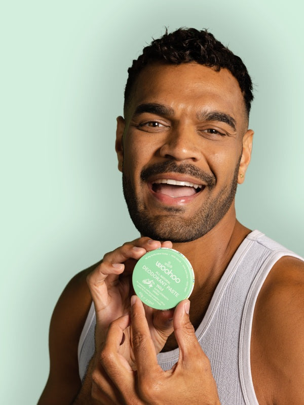 Smiling man holding WooHoo Wild natural deodorant paste beside his face