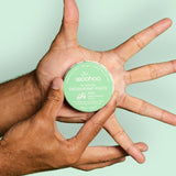 WooHoo Wild deodorant paste held between several hands on a green background