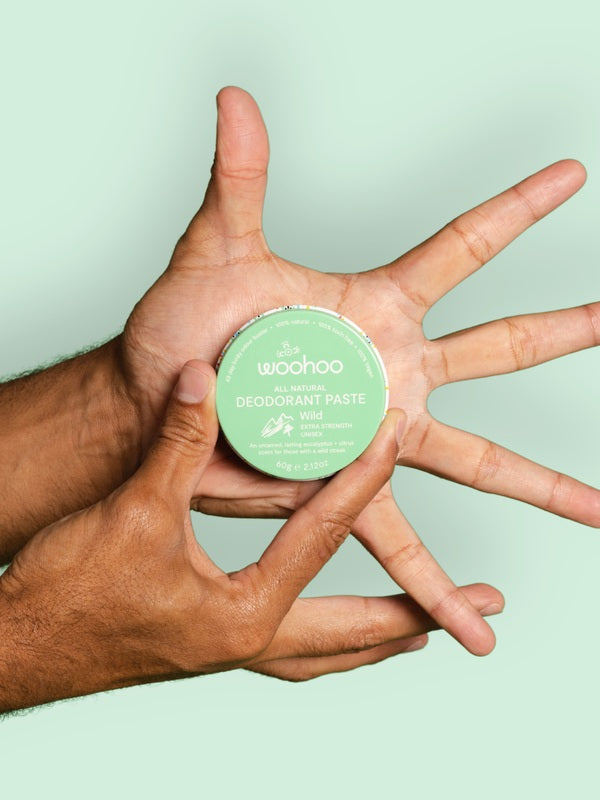 WooHoo Wild deodorant paste held between several hands on a green background
