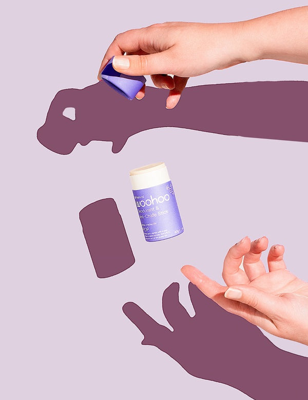 Hands opening a WooHoo Pop natural deodorant stick against a purple background